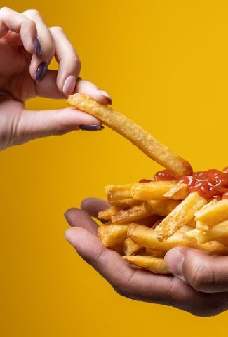 Healthy Fast-Food Close Up of a Person's Hands One with Fries and Ketchup and the Other Pulling a Single Fry from the Other